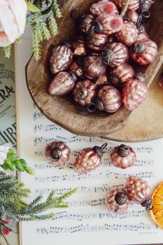 a wooden bowl filled with lots of different types of beads next to an orange on top of sheet music