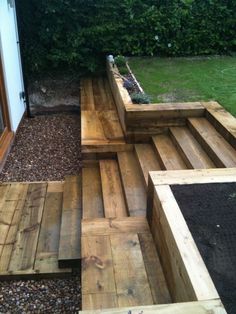 a wooden bench sitting in the middle of a garden area next to a door and grass