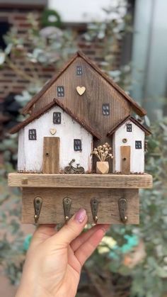 a hand holding a small wooden house on a shelf with key hooks and keys attached to it