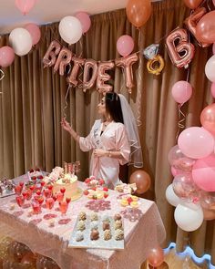 a woman standing in front of a table filled with cakes and cupcakes next to balloons