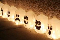 lighted bottles with faces and eyes are lined up in a row on the ground, all decorated to look like ghostes