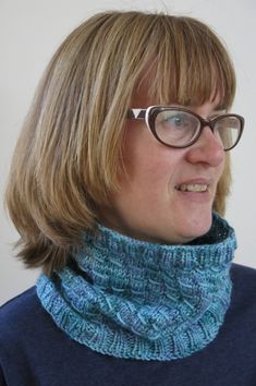 a woman wearing glasses and a knitted cowl neck scarf in teal blue