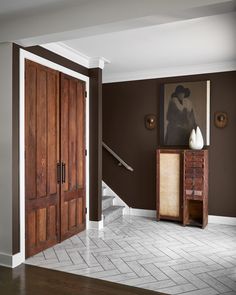 a living room with brown walls and white tile flooring on the ground, two wooden doors leading to an entry way