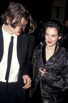 a man in a suit and tie standing next to a woman wearing a leather jacket