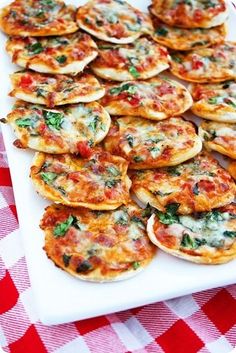 small pizzas with spinach and cheese are arranged on a white platter atop a checkered tablecloth