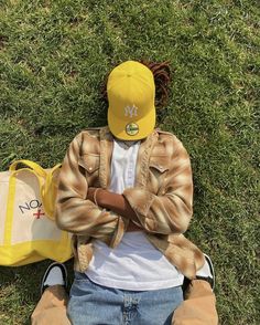 a person wearing a yellow hat sitting in the grass with a bag on their lap