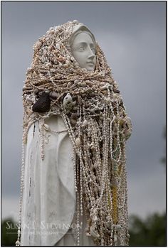 a statue covered in beads and chains on top of a white headdress against a cloudy sky