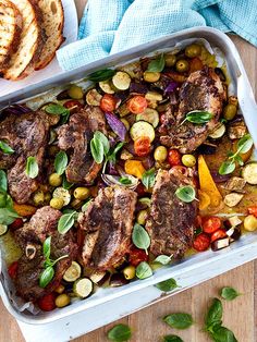 a tray filled with meat and vegetables on top of a wooden table next to bread