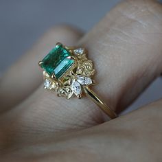 a close up of a person's hand holding a ring with an emerald and diamond