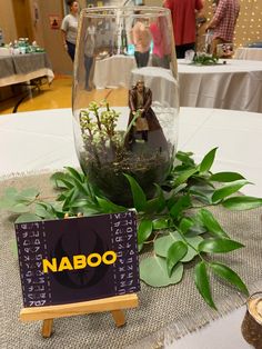 a table topped with a glass vase filled with water and plants next to a sign that says naboo