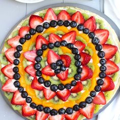 a fruit pizza with kiwis, strawberries and blueberries on top is shown