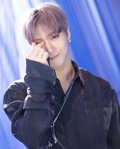 a young man posing for a photo in front of a blue curtain with his hand on his face