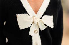 Our cardigan features a sophisticated color contrast design, with black as the base color complemented by elegant cream detailing along the neckline. This contrast adds a touch of refinement and visual interest, making it a versatile piece for both professional and casual settings. One of its standout features is the delicate bow embellishment and is adorned with pearl and gold buttons. Our Model Kristi is 5’8 and wearing a XS. She normally wears XS, 26, or 0.