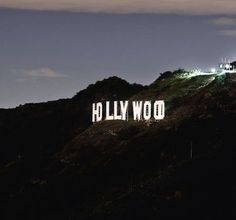 the hollywood sign is lit up at night on top of a hill with mountains in the background