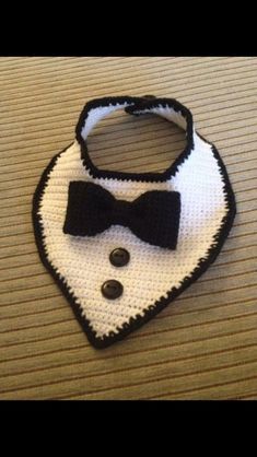 a crocheted bib with a black and white bow tie on it sitting on a table