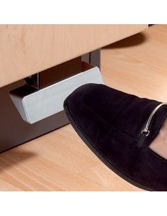 a person's foot wearing black slippers under a desk