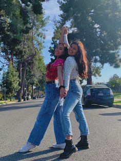 two girls are standing in the street with their arms around each other and one girl is holding her hand up