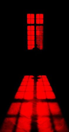 the shadow of a person standing in front of a window with red light coming through it