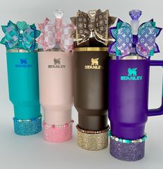 four different colored travel mugs with bows on the top and bottom one is pink, purple, blue, and green