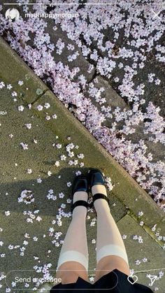 a person wearing black shoes standing on top of a sidewalk with pink flowers in the air