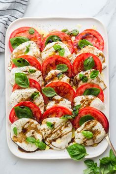 mozzarella and tomato salad on a white platter, with basil leaves around it