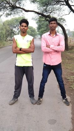 two young men standing next to each other on a road with trees in the background