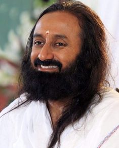 a man with long hair and a beard wearing a white shirt smiles at the camera