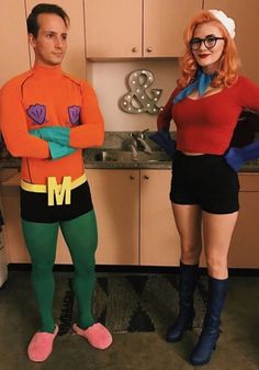 two people dressed up in costumes standing next to each other near an oven and stove top