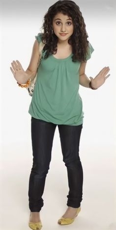 a young woman is standing with her hands in the air while wearing jeans and a green top