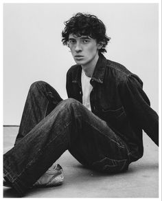 a young man sitting on the ground wearing jeans