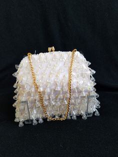 a white purse with gold chains on the front and bottom, sitting on a black surface