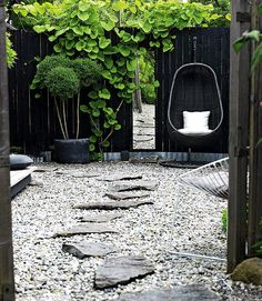 an outdoor area with rocks and plants in the background, including a hanging egg chair