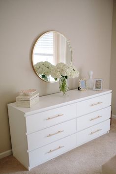 a white dresser with flowers and a round mirror