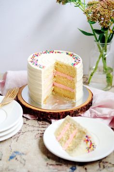 a white cake with pink frosting and sprinkles sits on a table