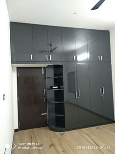 an empty room with black cabinets and wood flooring in front of a ceiling fan