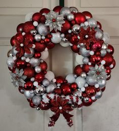 a red and white christmas wreath hanging on the front door with silver ornaments around it