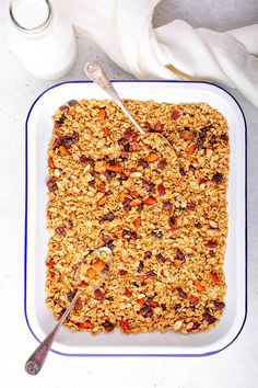 a square white plate topped with granola next to a glass container and spoons