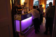 a group of people standing at a bar in a room with purple lighting on it