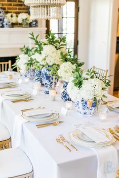 the table is set with blue and white dishes, gold place settings, and floral centerpieces