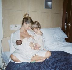 a woman holding a baby while sitting on top of a bed