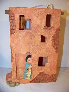 a clay house with two windows and a doll in it