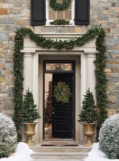 the front door is decorated with christmas wreaths and potted trees