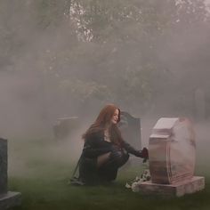 a woman kneeling down next to a box in the grass with fog on it and trees behind her