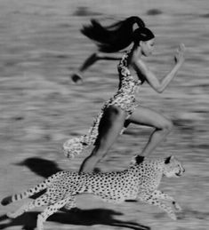 a woman is running with a cheetah in the desert while another runs behind her