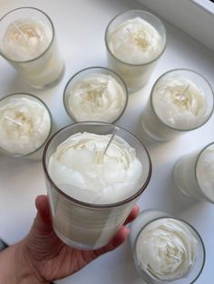 a hand holding a glass filled with whipped cream surrounded by small cups on a table