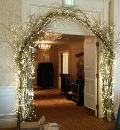 an archway decorated with branches and lights in a hallway at christmas time, next to a white door