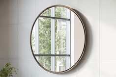 a round mirror hanging on the side of a wall next to a potted plant