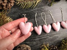 someone is holding some pink heart shaped ornaments in front of pine cones and evergreen needles