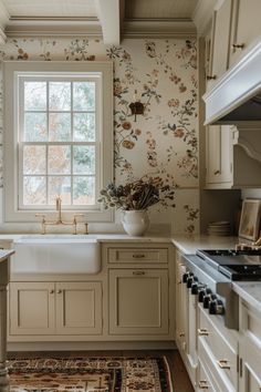 a kitchen with white cabinets and floral wallpaper on the walls, along with a large window