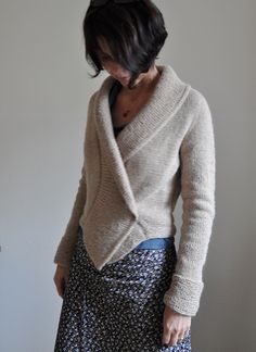 a woman standing in front of a white wall wearing a skirt and cardigan sweater